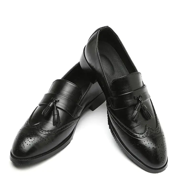 A pair of elegant burgundy leather loafers with a glossy finish. The shoes feature gold-toned metal horsebit detailing across the uppers and are displayed with wooden shoe trees inserted. They have a sleek, elongated silhouette with subtle stitching along the toe cap. The loafers are placed on a dark surface, partially framed by a wooden picture frame, emphasizing their classic and sophisticated style.