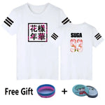 A white short-sleeve graphic T-shirt shown from both the front and back. The front features a square black-bordered design with bold black Asian characters over a pink floral pattern, while the back displays the name “SUGA” in black above the number “93” in a pink floral print. Both sleeves have three black stripe accents. At the bottom, the image also shows free gift items: a blue-and-pink wristband and a round character pin badge.