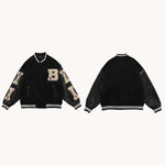 Front and back view of a black varsity jacket with striped ribbed collar, cuffs, and hem, featuring beige letter patches (including a large “B”) and contrasting sleeves, shown on a light background.