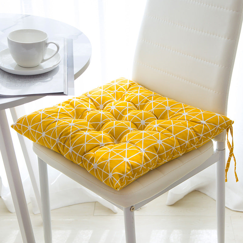 Yellow geometric patterned chair pad on a white chair with a cup and saucer in the background.