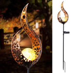 Decorative solar garden stake light with a tall gold flame-shaped metal design and cutout patterns, holding a glowing orb; shown lit outdoors at night and as a full product view on a white background.