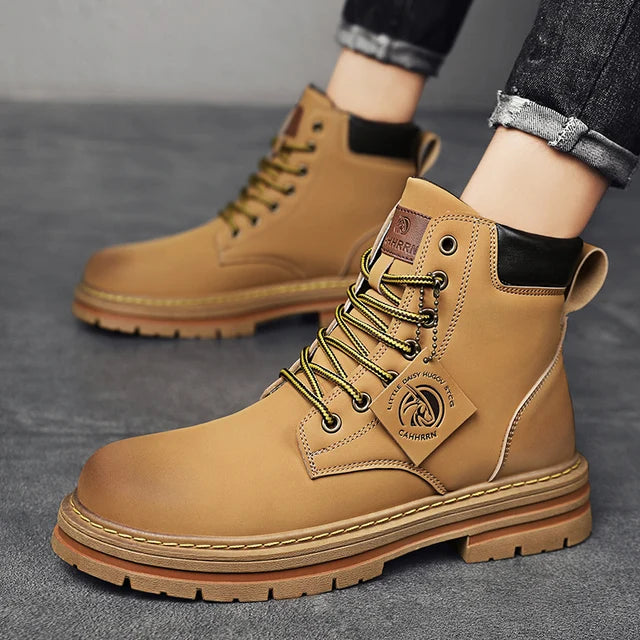 A pair of sleek black leather ankle boots with rugged rubber soles, lace-up fronts, and metal eyelets, displayed on a gray fabric surface with one boot propped up on a vintage-style book for presentation.