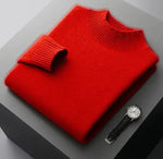 A neatly folded beige knitted sweater with a ribbed high collar and cuffs, placed on a dark grey surface. Beside the sweater, a classic wristwatch with a black leather strap and a silver dial is positioned, adding a touch of elegance to the composition.