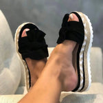 Black bow-detail wedge slide sandals with braided espadrille-style platform soles.
