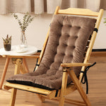 Wooden chair with a brown cushion on a wooden floor, with a small table and plants in the background.