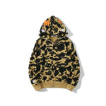 Camouflage zip-up hoodie in tan and dark green with a shark-face design on the hood, including embroidered eyes and orange lettering.