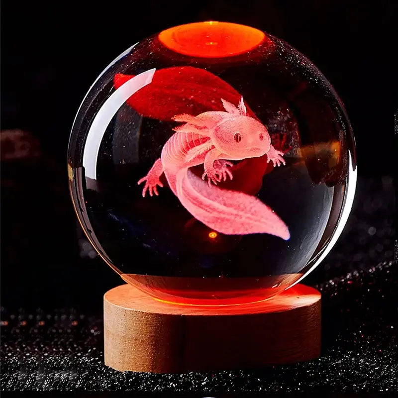 Glowing crystal ball on a wooden base, illuminated in red-orange and engraved with a 3D-style axolotl-like salamander inside, set against a dark background with sparkly reflections.
