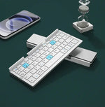 Foldable white wireless keyboard on a desk beside a phone and hourglass.