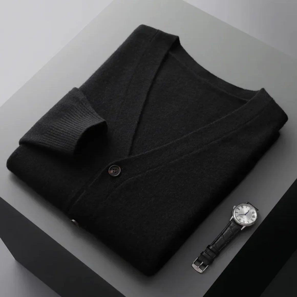 A neatly fold shirt on a black  surface with a black leather wrist-watch beside it