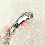 This image shows a handheld electric hair/scalp brush (a massaging/therapy brush):

A person is holding a curved, ergonomic brush.

The underside has soft silicone bristles (the pink/red nubs), designed to massage the scalp and help distribute shampoo or treatment oils.

The top looks like a smooth plastic housing, consistent with electric vibration/heat/light therapy style scalp brushes.

The green speckled pattern across the image appears to be digital noise/compression artifacts or an overlay, not part o