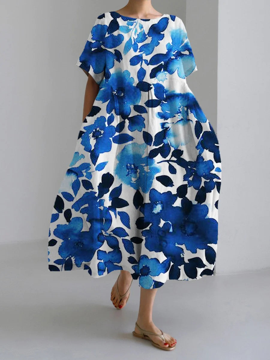 Woman wearing a loose-fitting, white midi dress with short sleeves, featuring bold red-orange floral prints accented with blue centers, paired with flat sandals.