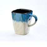 Blue and white glazed ceramic mug with an angular shape and curved handle.
