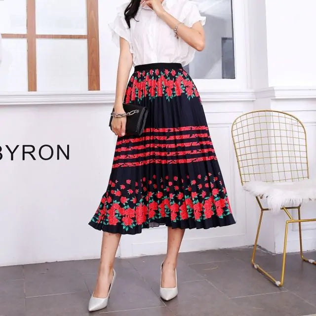 Pleated midi skirt with a gradient design, transitioning from dark black at the waistband to a soft blush pink at the hem, hanging on a black clothing rack next to a vintage-style camera.