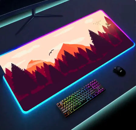 RGB-lit extended gaming mouse pad on a desk, featuring a stylized mountain-and-forest landscape design, with a keyboard and mouse placed on top.