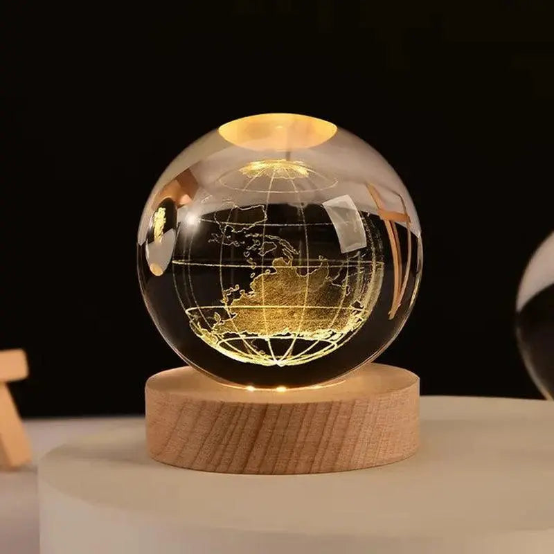 A clear crystal globe with a gold-etched world map, glowing from a warm LED light, resting on a round wooden base on a tabletop against a dark background.