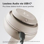 Close-up promotional image of beige Beats over-ear headphones showing the earcup and USB-C cable connection, with text reading “Lossless Audio via USB-C” and “Plus three distinct built-in sound profiles