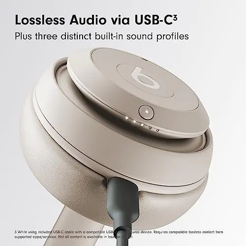 Close-up promotional image of beige Beats over-ear headphones showing the earcup and USB-C cable connection, with text reading “Lossless Audio via USB-C” and “Plus three distinct built-in sound profiles