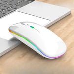 White wireless computer mouse with a rainbow LED light strip around the base, shown next to a laptop on a wooden desk.