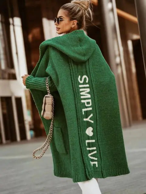 Woman wearing a green cardigan with 'Simply Live' text, walking outdoors.