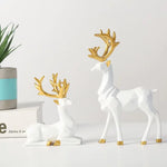 Two white geometric deer figurines with gold antlers and gold hoof accents displayed as home décor.