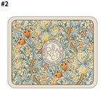 Rectangular decorative mat with a cream border, ornate vintage botanical pattern in soft blues, greens, and warm floral tones, and a central circular emblem with stylised lettering.