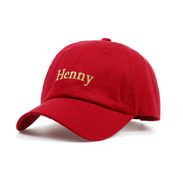 A studio product photo of a red baseball cap on a white background, featuring curved brim and gold embroidered text on the front that reads “Henny.