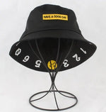 Black bucket hat displayed on a wire stand, with a yellow patch reading “HAVE A GOOD DAY” on the front and white numbers printed around the brim.