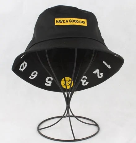 Black bucket hat displayed on a wire stand, with a yellow patch reading “HAVE A GOOD DAY” on the front and white numbers printed around the brim.