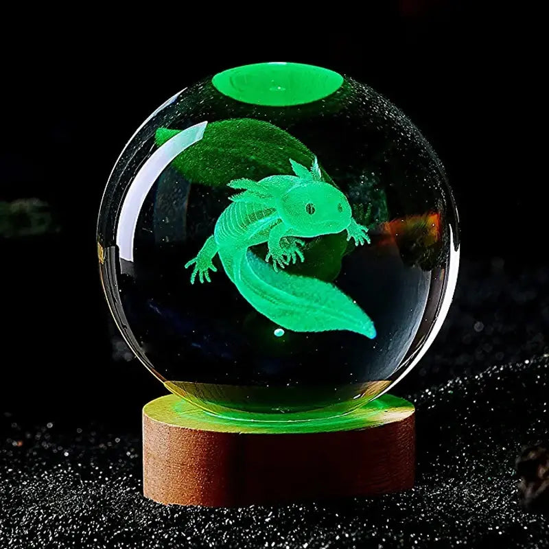 The image shows a glowing 3D-etched model of an axolotl inside a crystal ball, illuminated in green with a wooden base. The intricate details of the axolotl's shape and features are highlighted, creating a stunning visual effect.