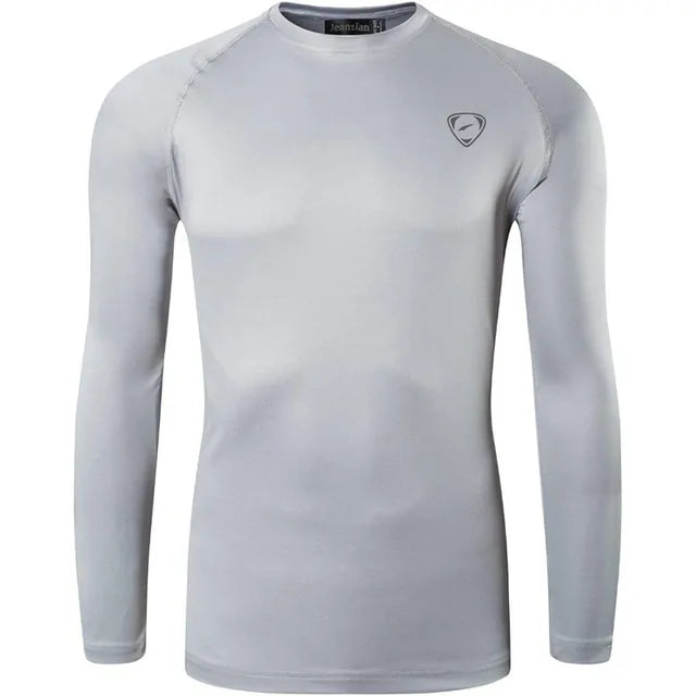 A sleek, light gray long-sleeve compression shirt with a crew neck, featuring a small logo on the upper left chest. The fabric appears smooth and stretchy, designed for athletic or casual wear.