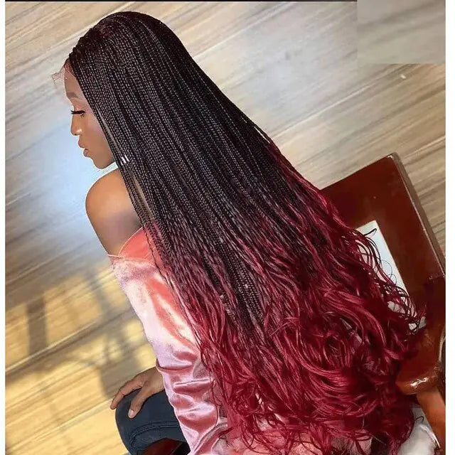 A person with long braided hair that transitions from black at the roots to a deep red at the ends, styled in loose waves. They are wearing a light pink shirt, and the photo is taken from the back, showing the full length of the hair.