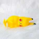A small yellow Pikachu figurine lying on its side on a fluffy white surface, with closed eyes, red cheeks, and black-tipped ears.