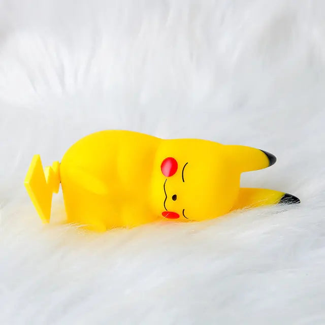 A small yellow Pikachu figurine lying on its side on a fluffy white surface, with closed eyes, red cheeks, and black-tipped ears.