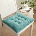 Teal textured chair pad on a white chair with a small table in the background.