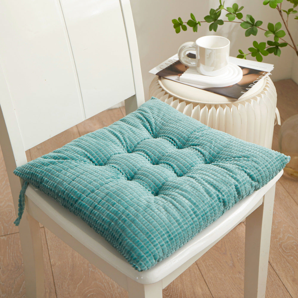Teal textured chair pad on a white chair with a small table in the background.