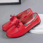 A pair of red slip-on loafers with moc-toe stitching, decorative bow laces, side cutout accents, and black flexible driving-style soles.