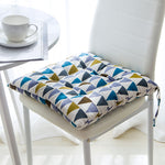 Colorful geometric patterned seat cushion on a chair with a white table and cup in the background.