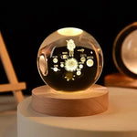 A glass globe featuring an engraved depiction of the solar system, with planets and an astronaut in space, illuminated with soft lighting.