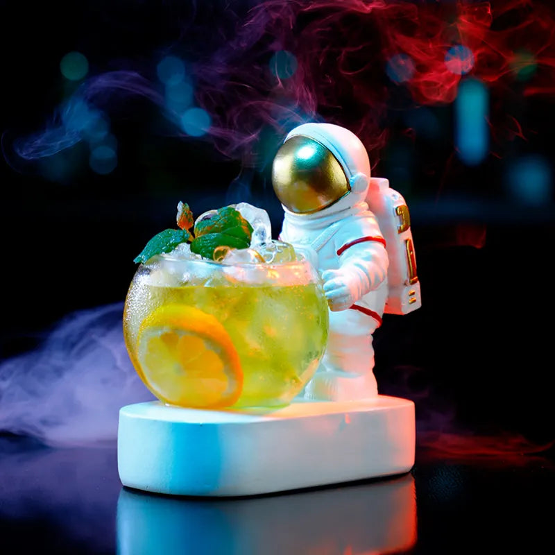 Astronaut-shaped drink holder beside a lemon cocktail with colourful smoky lighting.