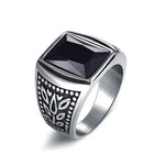 A silver signet-style ring with a square black gemstone and an engraved patterned side, shown on a white background.