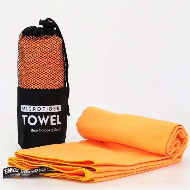 Bright orange microfiber towel shown folded and rolled beside a black mesh drawstring pouch labeled “MICROFIBER TOWEL – Beach • Sports • Travel,” on a white background.