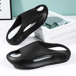 A pair of stylish black slip-on sandals with purple cushioned insoles, featuring cutout designs on the sides and toes, displayed on a white surface next to stacked books.