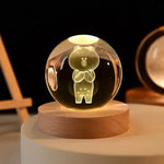 Illuminated crystal globe with a 3D laser-etched bear character inside, standing with arms crossed, mounted on a wooden base, glowing with a soft yellow light against a dark background.