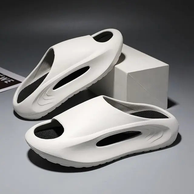 A pair of stylish black slip-on sandals with purple cushioned insoles, featuring cutout designs on the sides and toes, displayed on a white surface next to stacked books.