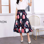 Pleated midi skirt with a gradient design, transitioning from dark black at the waistband to a soft blush pink at the hem, hanging on a black clothing rack next to a vintage-style camera.