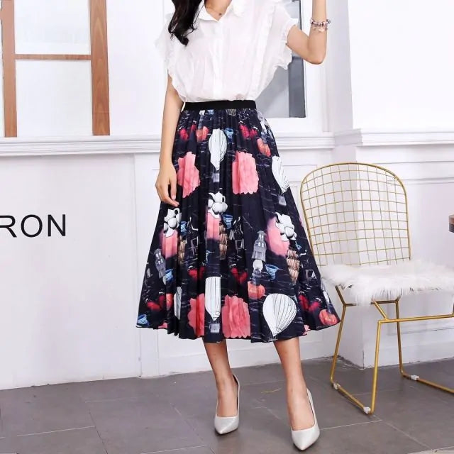 Pleated midi skirt with a gradient design, transitioning from dark black at the waistband to a soft blush pink at the hem, hanging on a black clothing rack next to a vintage-style camera.