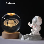 A glowing Saturn planet model inside a glass sphere on a wooden base, paired with a small white astronaut figurine on the moon.
