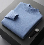 A neatly folded beige knitted sweater with a ribbed high collar and cuffs, placed on a dark grey surface. Beside the sweater, a classic wristwatch with a black leather strap and a silver dial is positioned, adding a touch of elegance to the composition.
