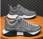Two gray lace-up sneakers with quilted panels and “AIR” text on the side, featuring white midsoles and chunky black tread, displayed on a wooden surface in front of a chain-link style background.