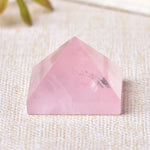 Pink rose quartz pyramid crystal on a beige textured surface.